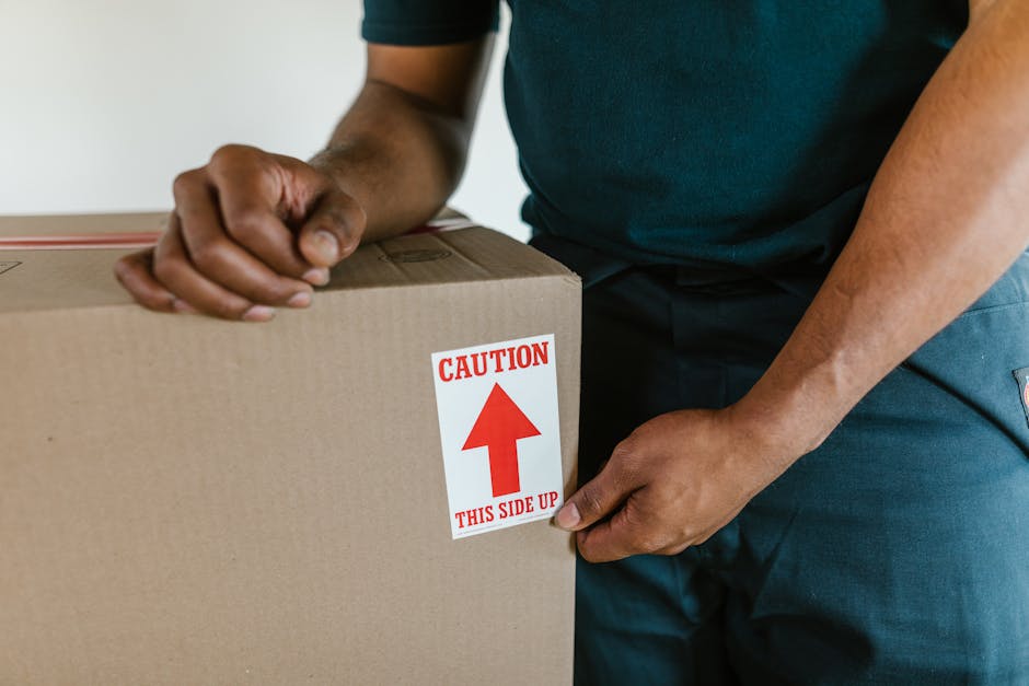 Close-up photograph of three brown cardboard moving boxes, stacked on a wooden floor inside a property. The top box has the handwritten label 'STUFF' in red marker, accompanied by a small, simple smil